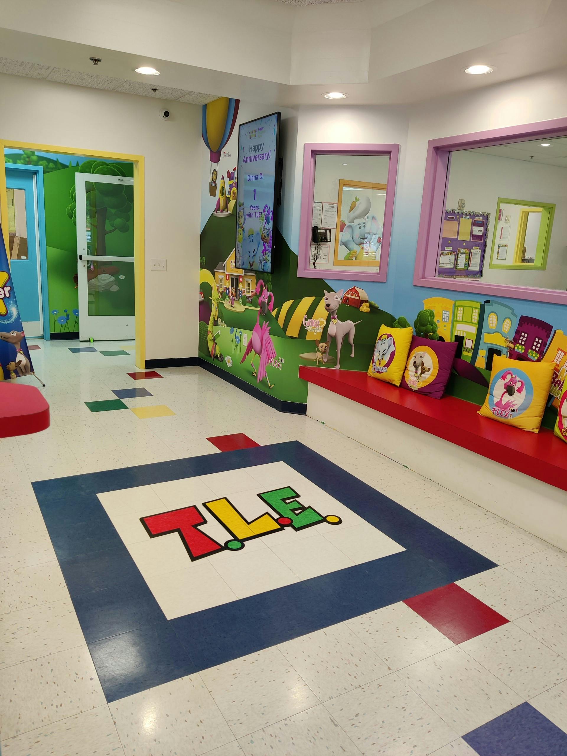 Playroom with colorful wall murals, red bench, and floor with "TLE" logo