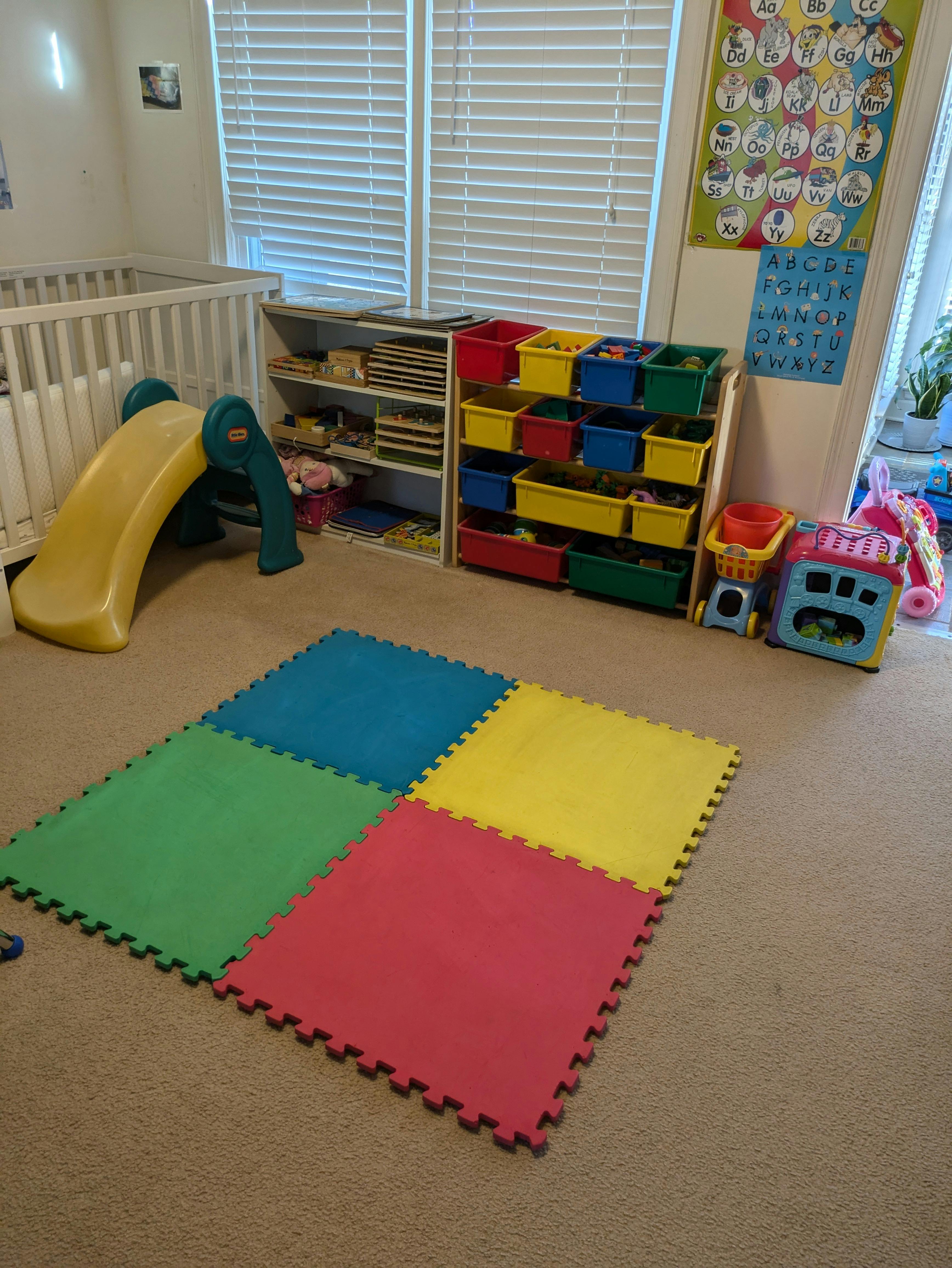 Playroom with a small slide, shelves of toys, and colorful foam floor mats