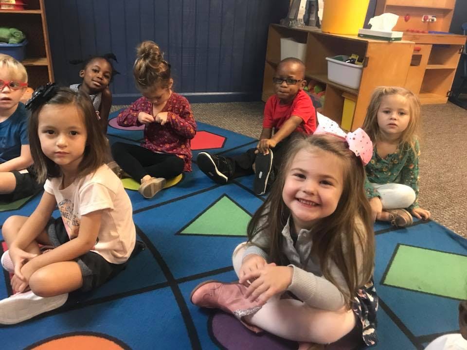Group of children sitting on a colorful rug in a classroom