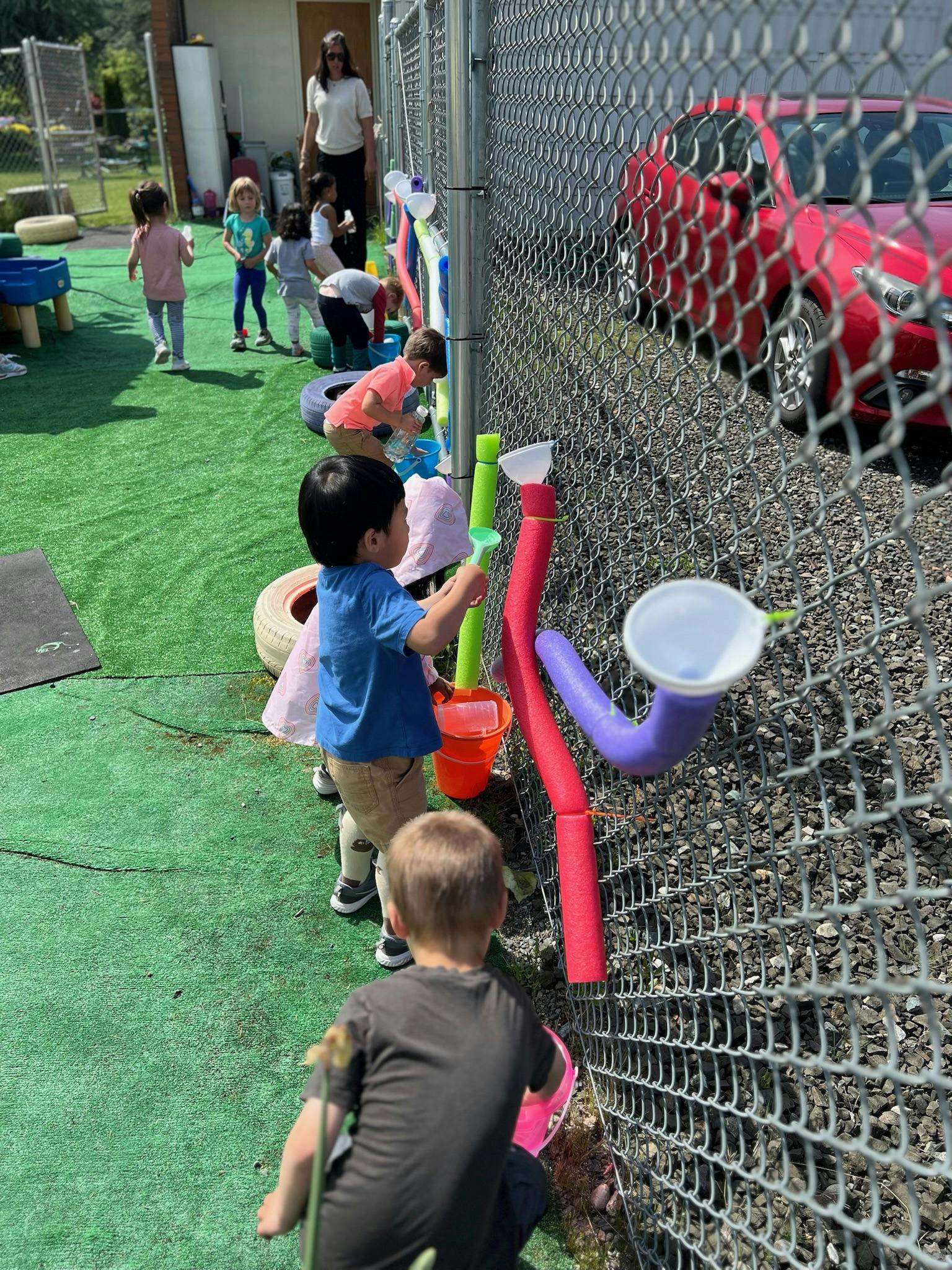Children playing with pool noodles and funnels attached to a fence