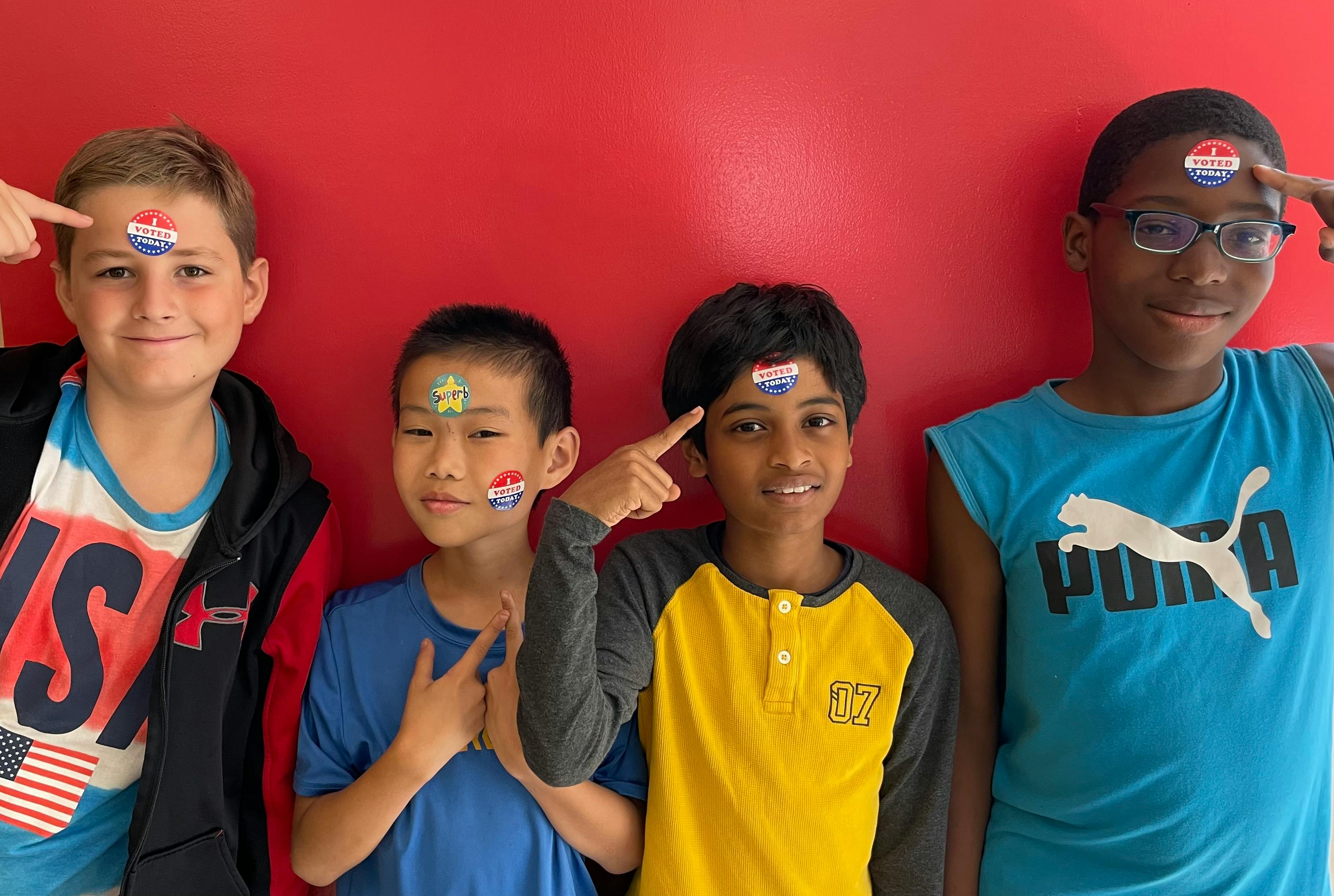 Four children pointing to stickers on their foreheads