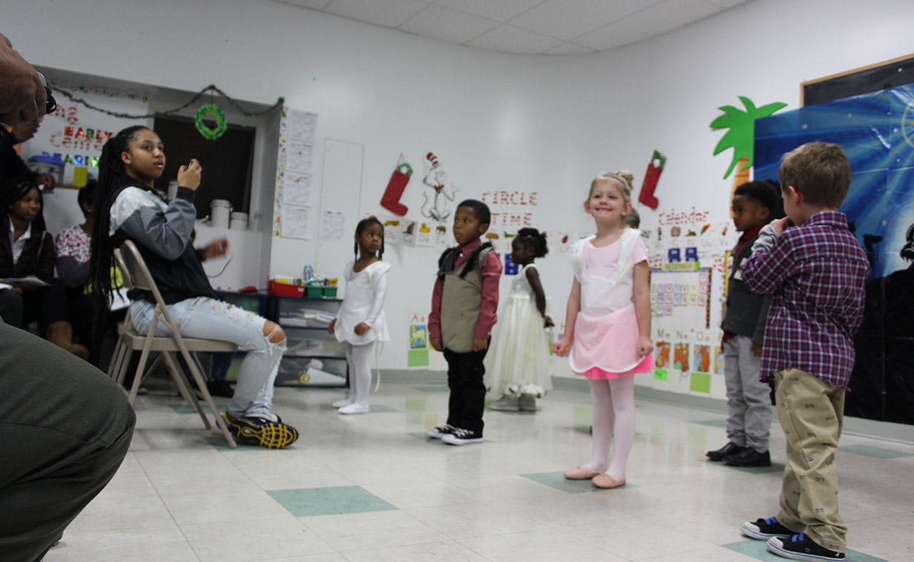 Person sitting on chair talking to children standing in a room