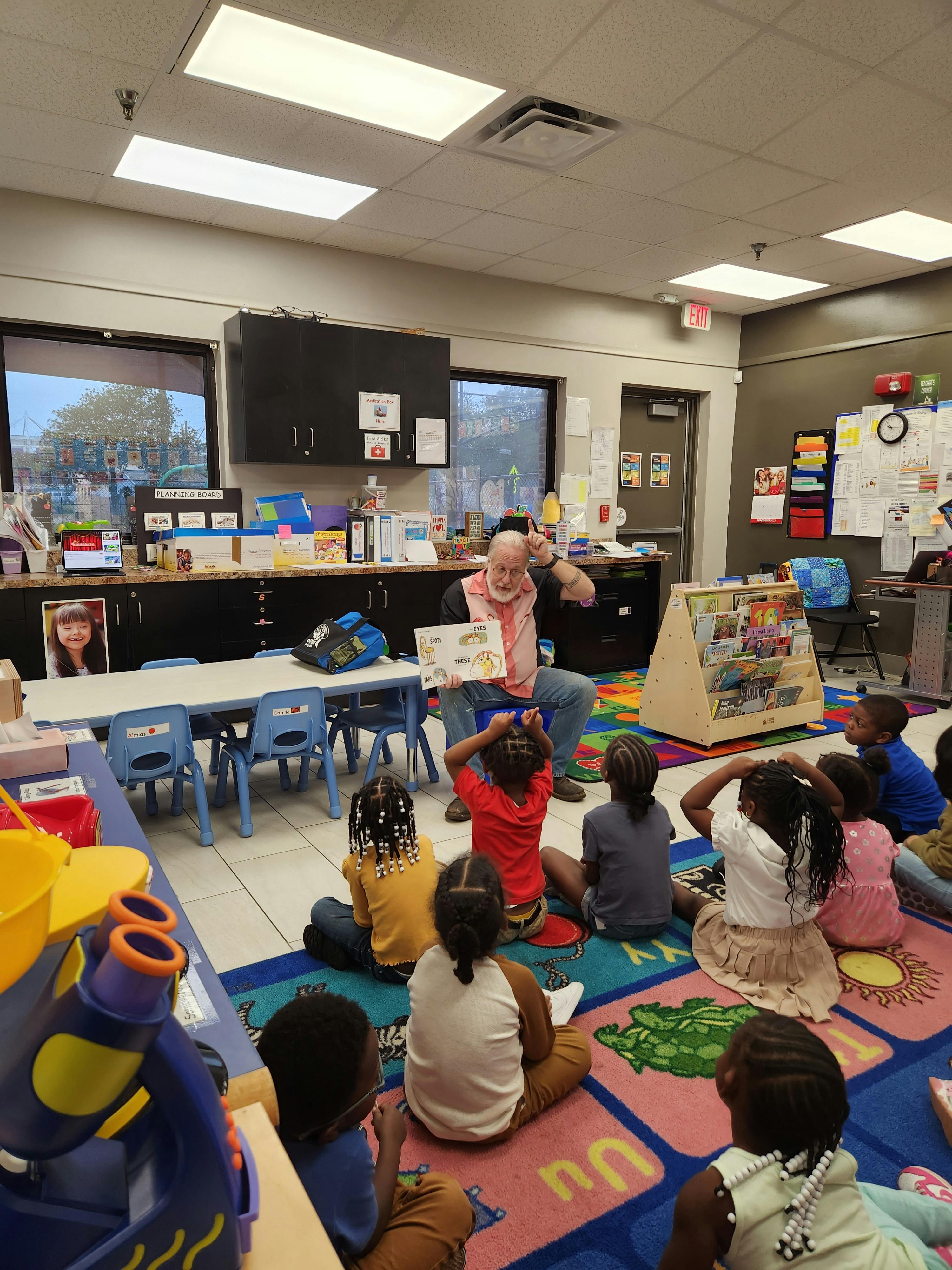 Adult person reading a book to several children in a classroom