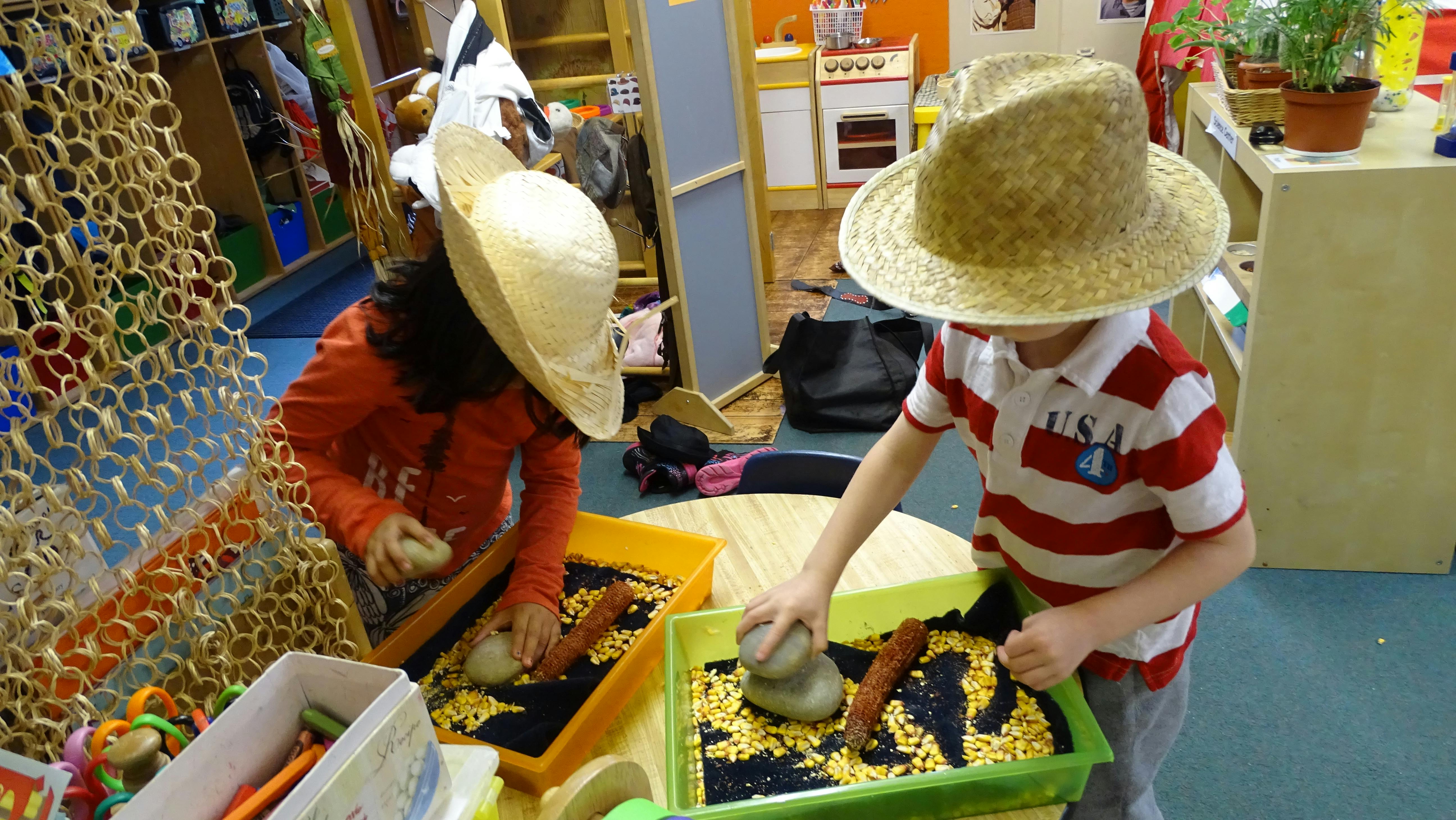 Two children wearing hats playing with beans and corn kernels in trays