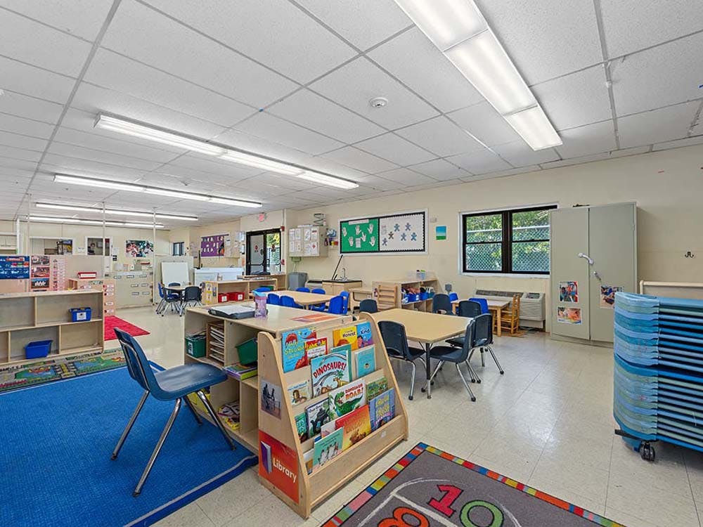 Empty classroom with small tables and chairs, a bookcase, and storage shelves
