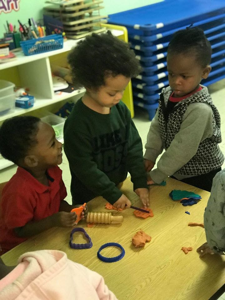 Three children playing with modeling clay at a table in a classroom