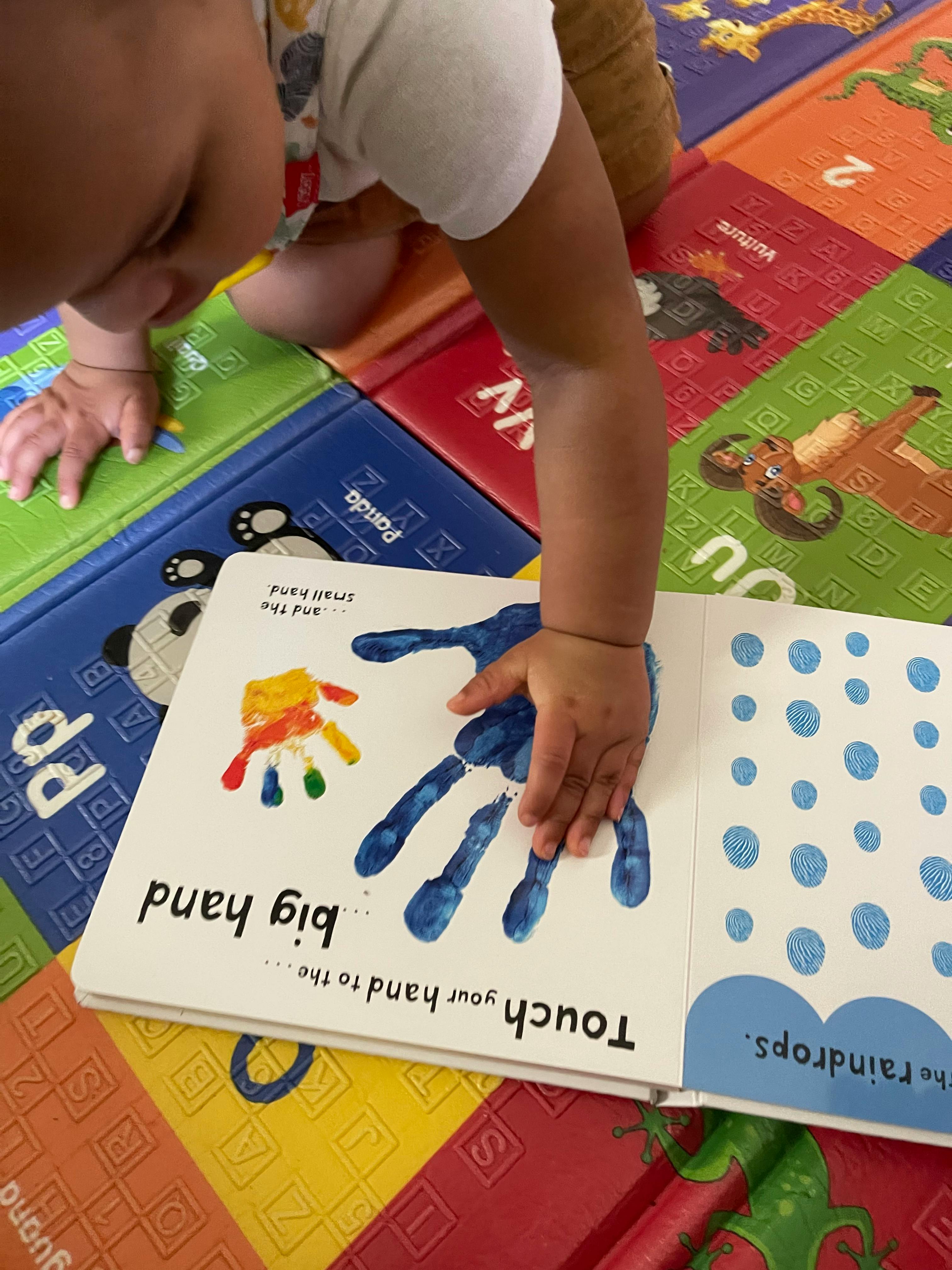 Child touching a book with a blue handprint and text "big hand"