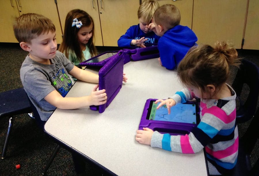 Children sitting at a table using tablets