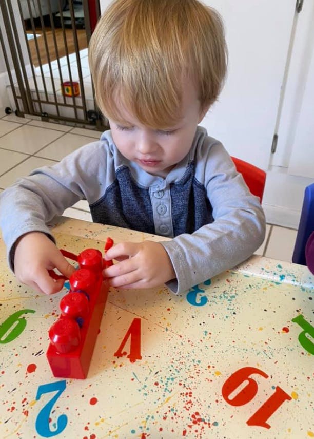 Child playing with a red toy on a table with numbers