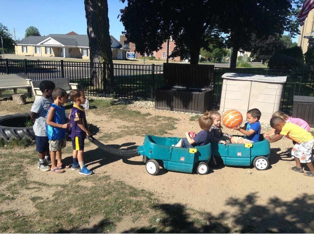 Children playing with toy wagons and a ball outdoors