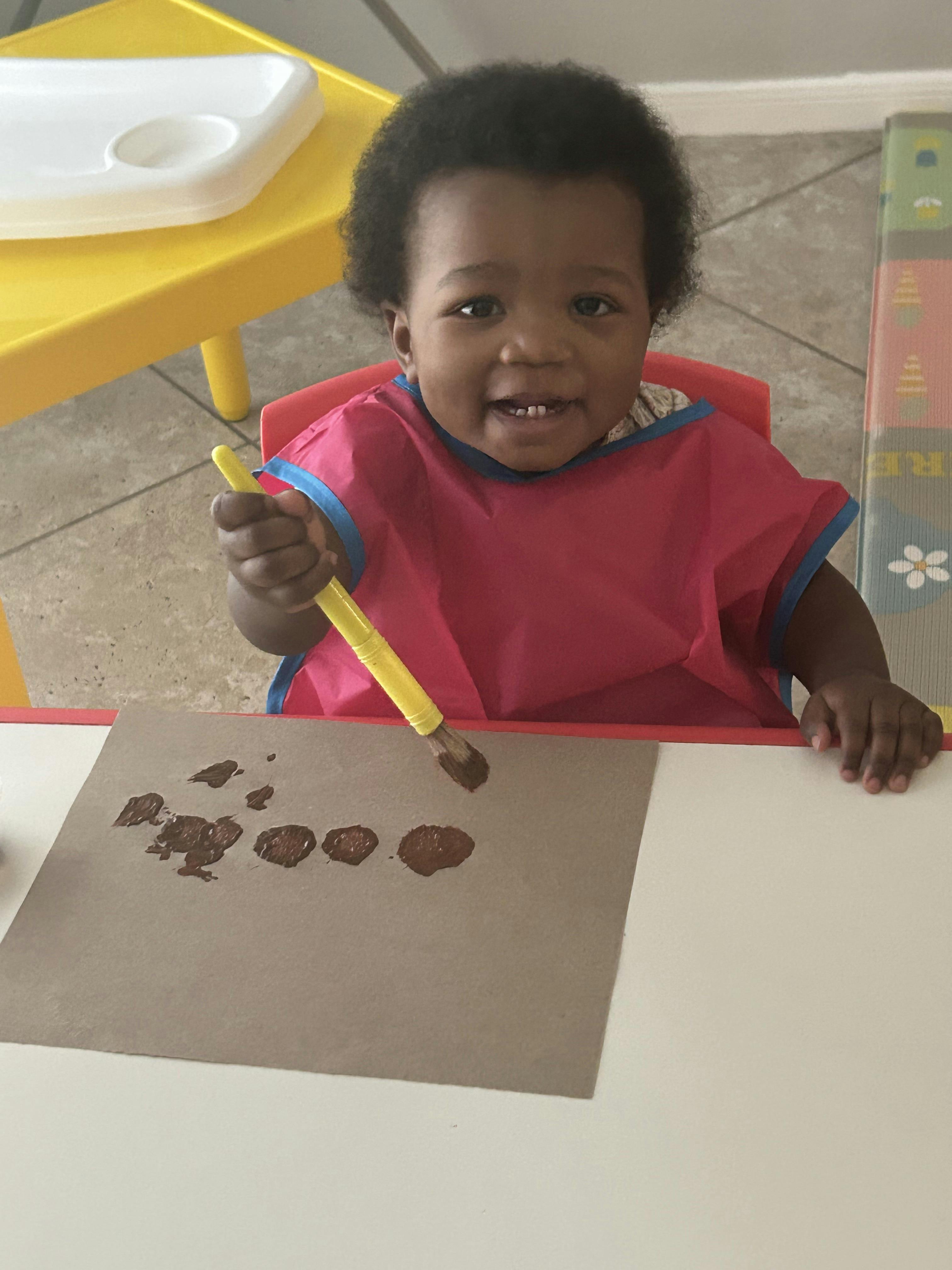 Child in a red bib painting with brown paint on paper