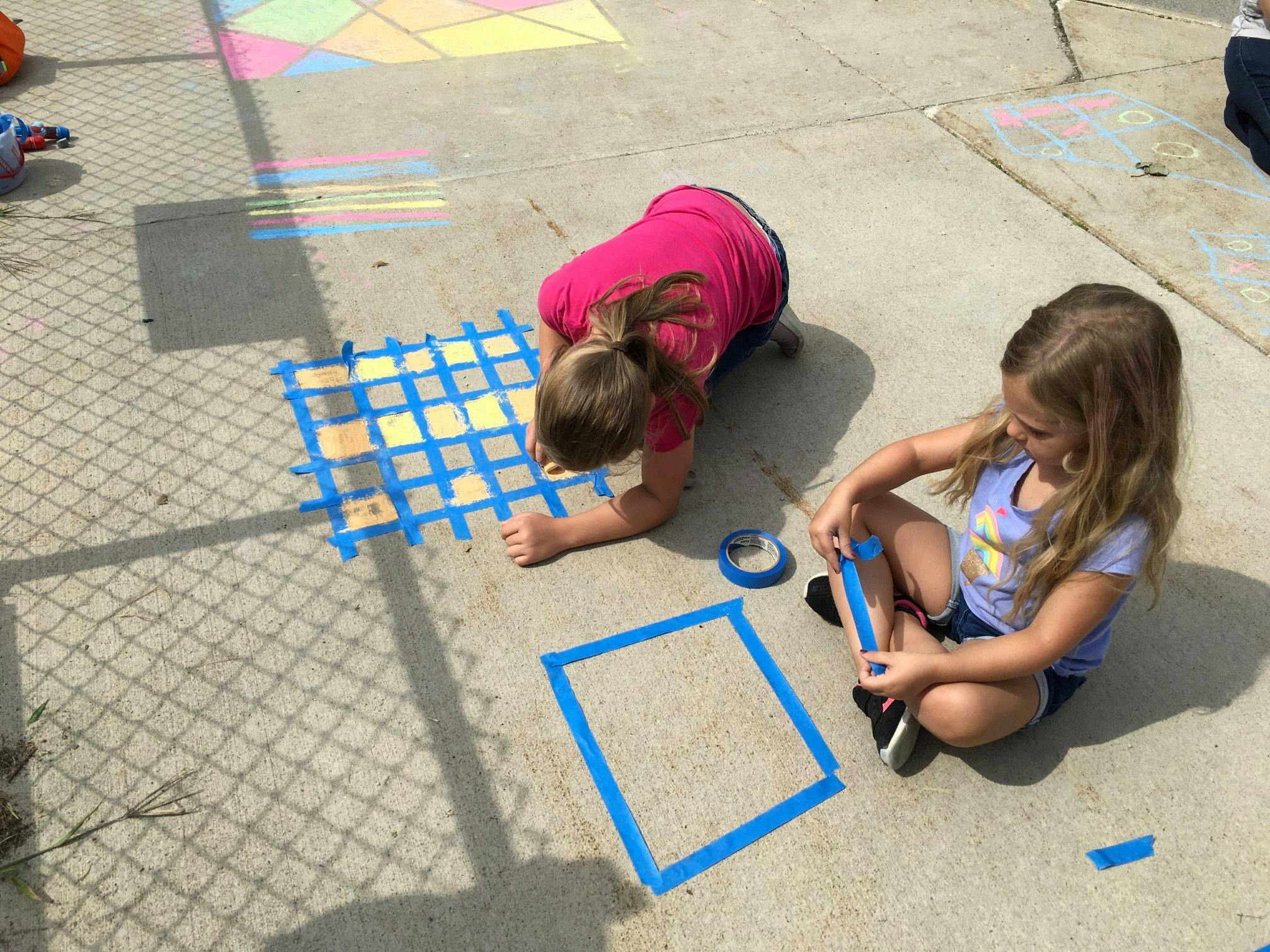 Two children creating art with tape on pavement