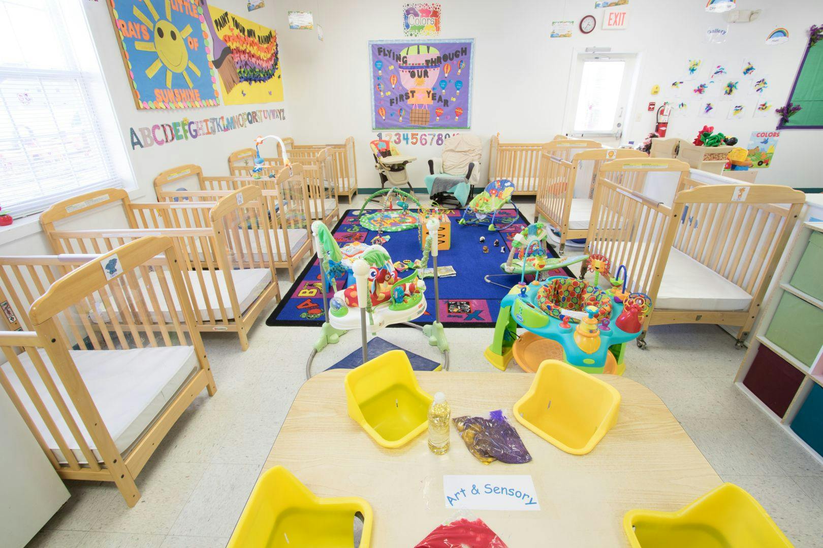 Nursery room with multiple cribs, play mats, and activity centers