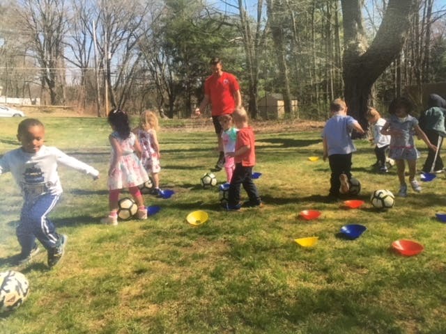 Children playing soccer outdoors with an adult supervising
