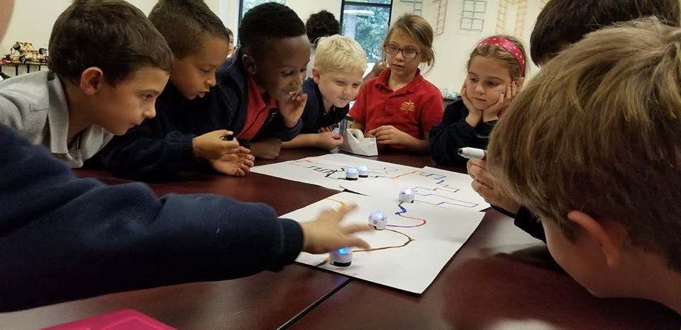Children gathered around a table looking at a paper with small robots