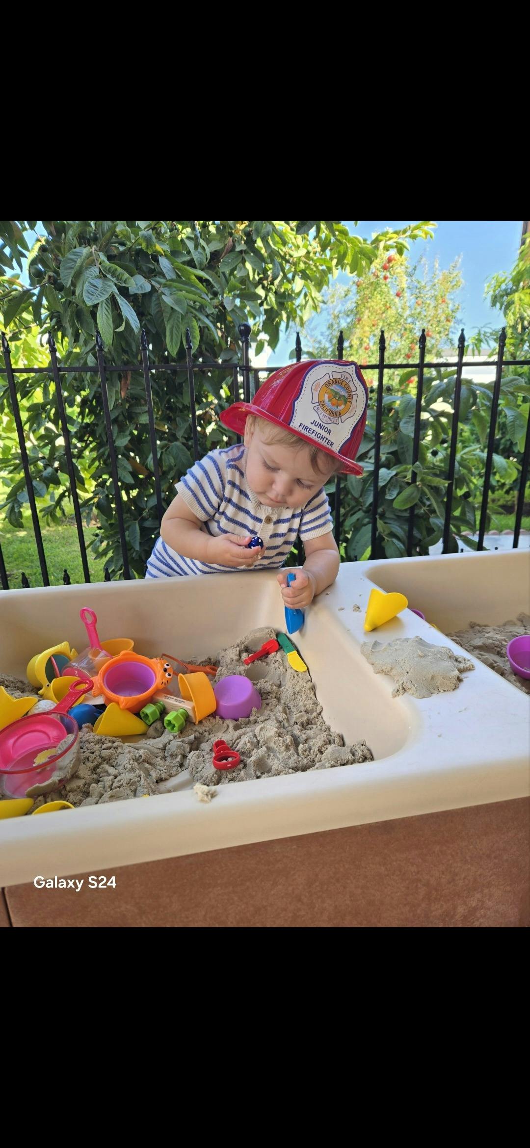 Child wearing a toy firefighter helmet playing in a sand table