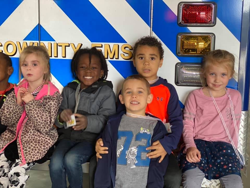 Group of children sitting in front of a vehicle with lights
