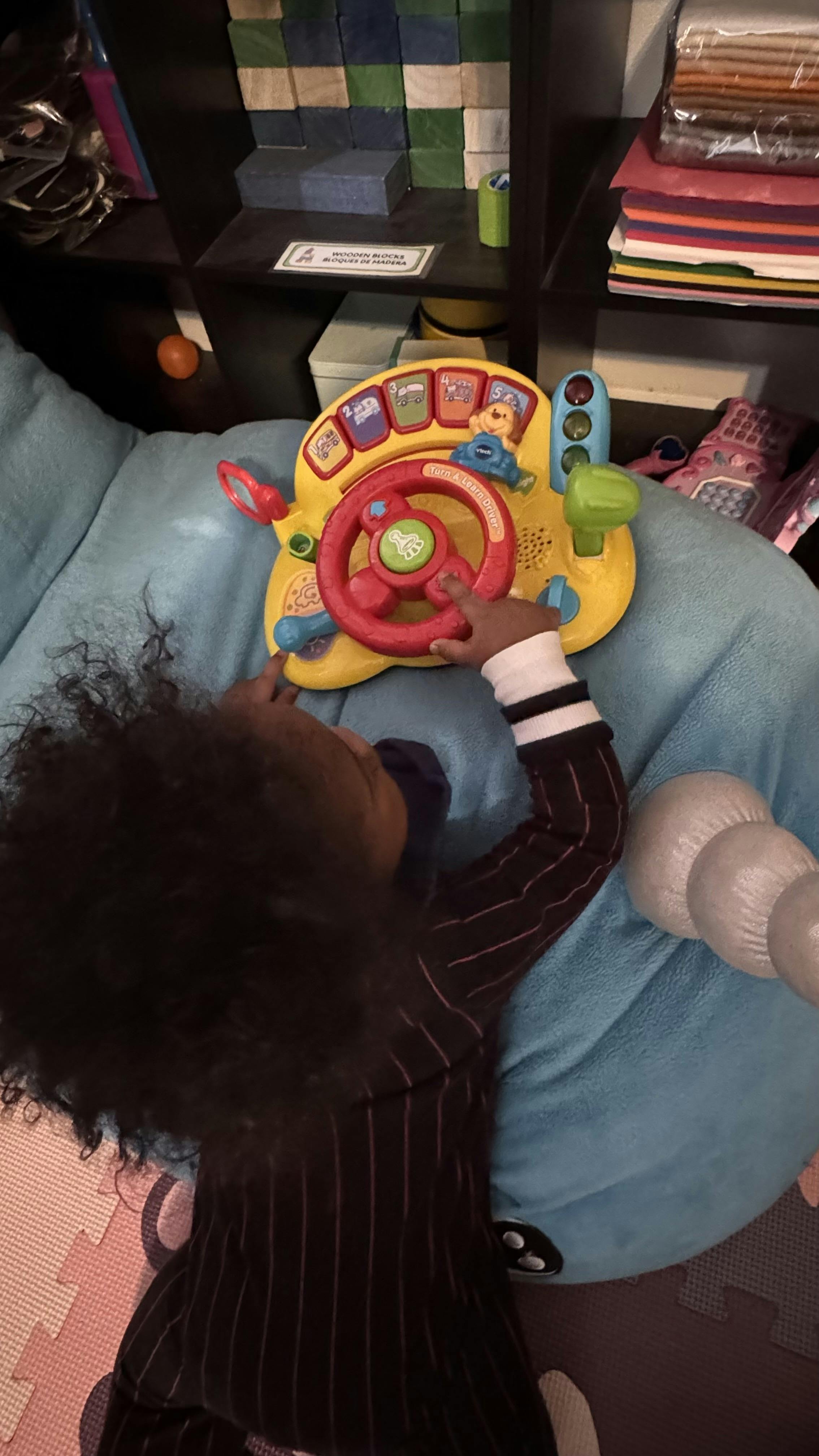 Child playing with a colorful toy steering wheel on a blue cushion