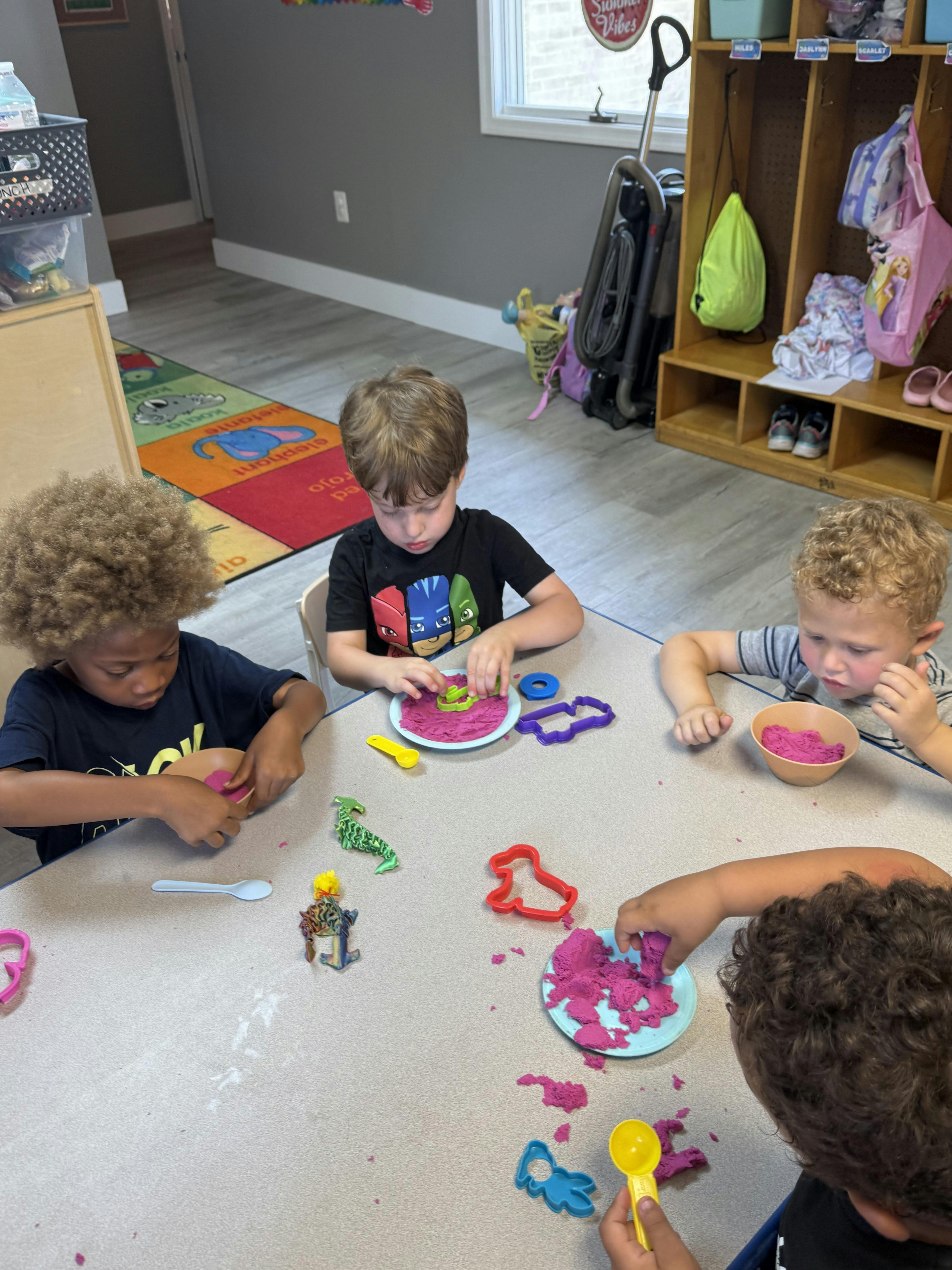 Four children playing with pink kinetic sand and plastic molds at a table