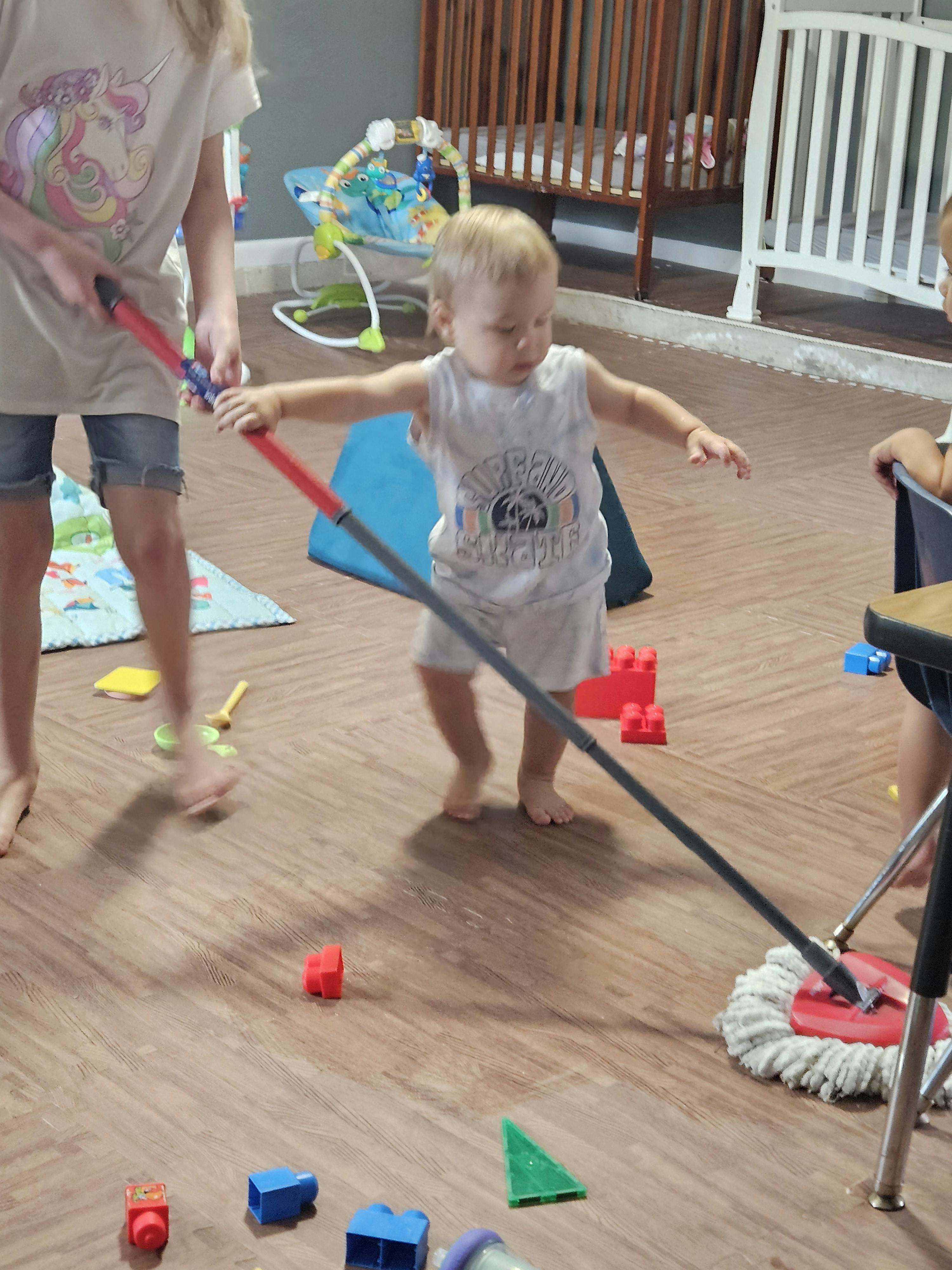 Child holding a mop with another person in the background