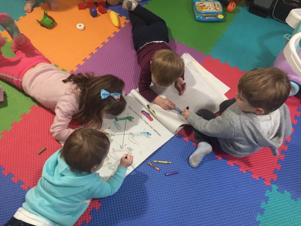 Four children drawing on a large sheet of paper on a colorful mat