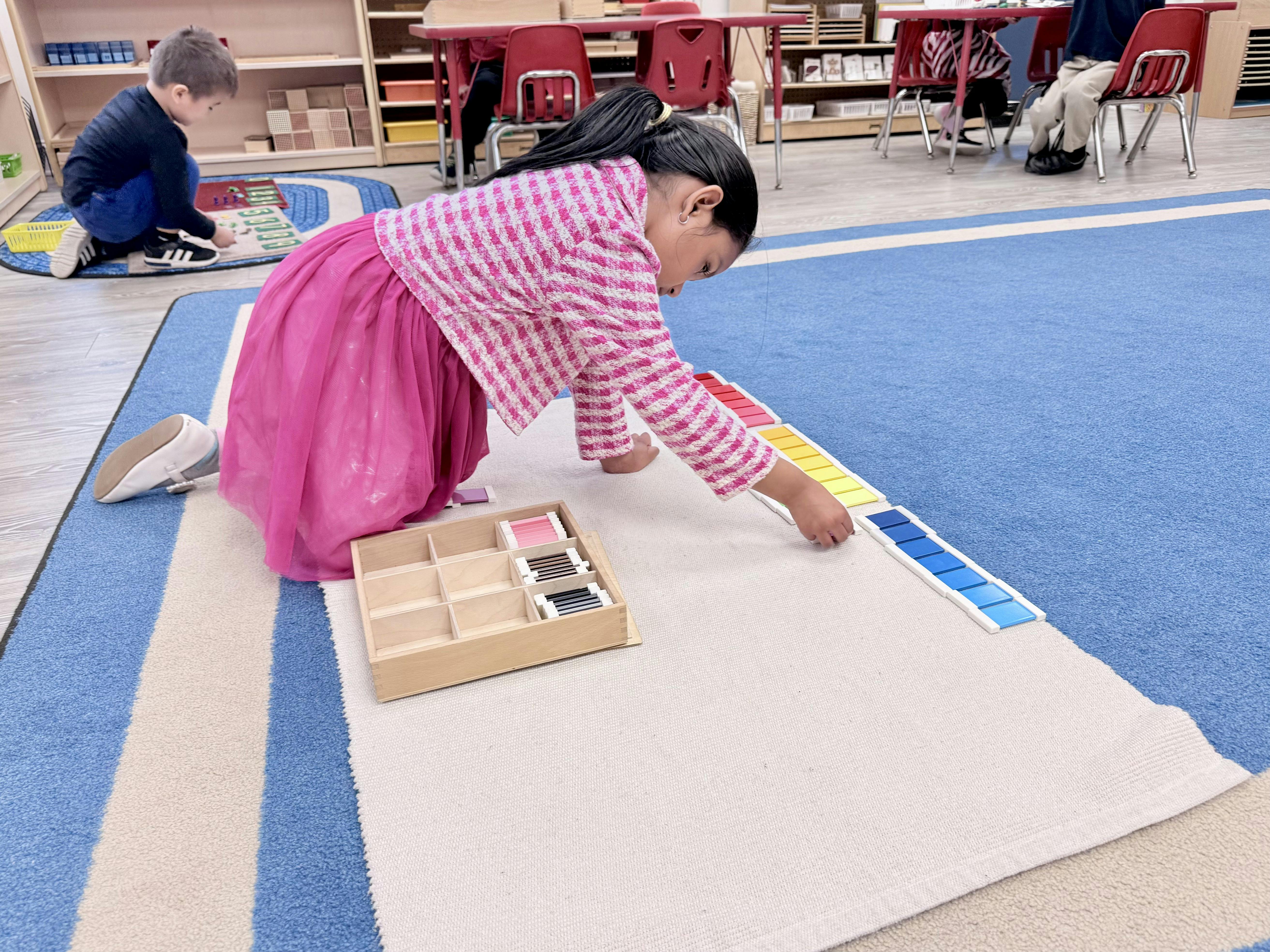 Child kneeling on a mat, arranging colored blocks in a classroom