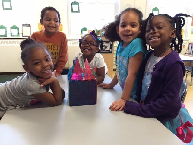 Five children smiling around a table with a craft project