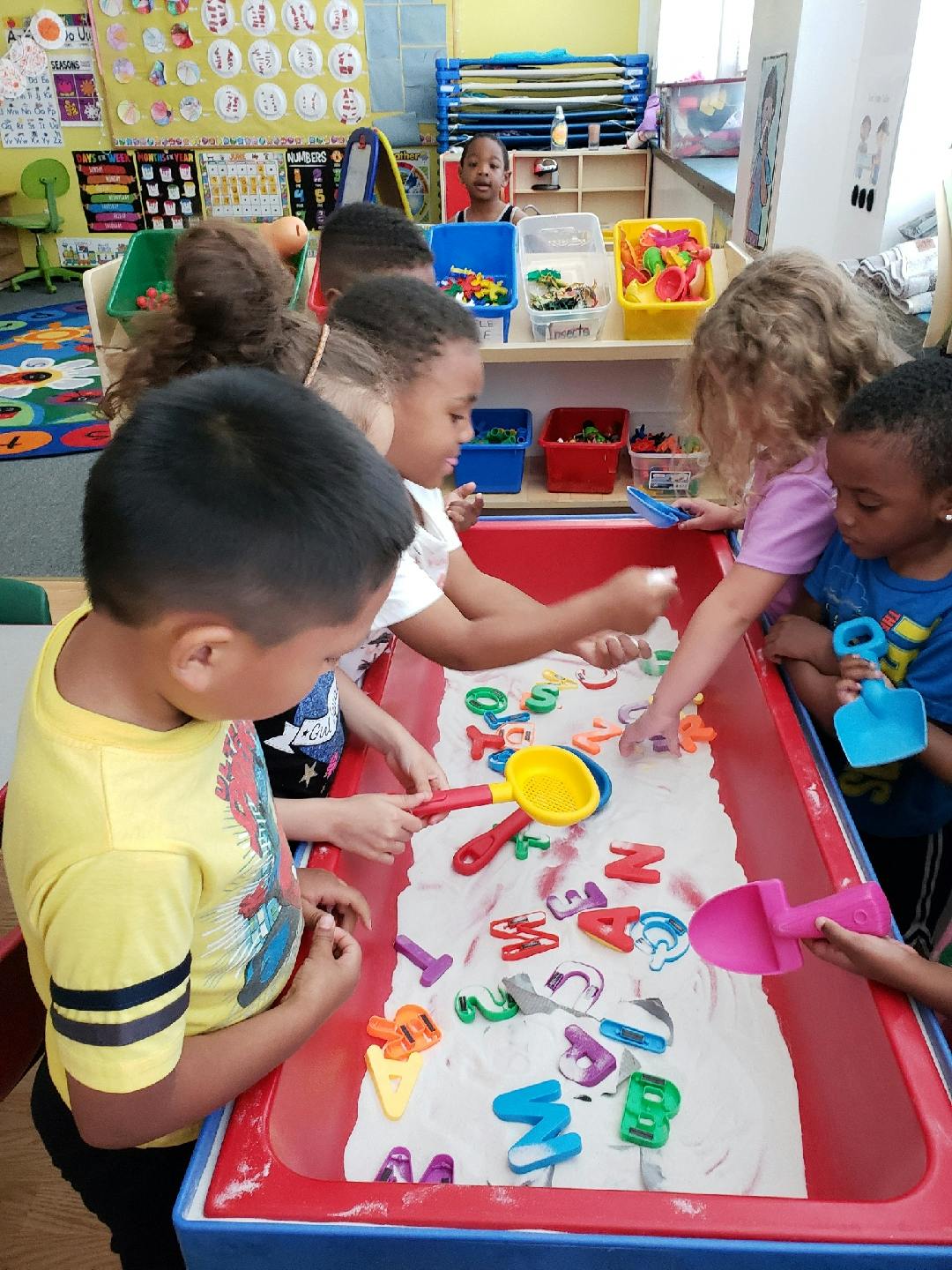 Children playing with alphabet letters in a sand table