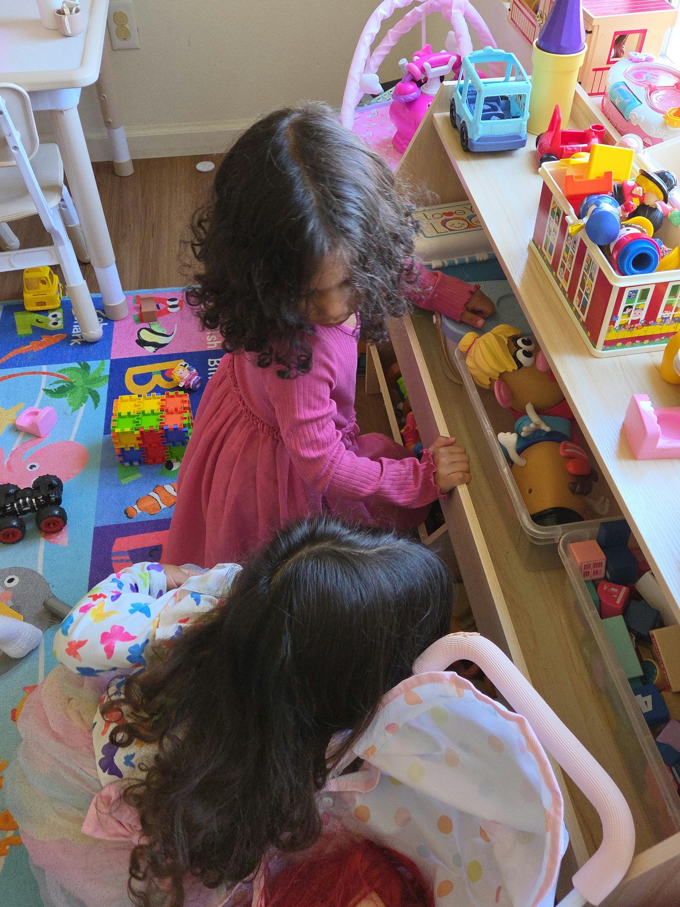 Two children reaching for toys on a shelf in a playroom