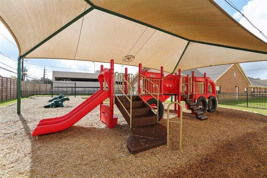 Red playground structure with slides and stairs under a shade canopy