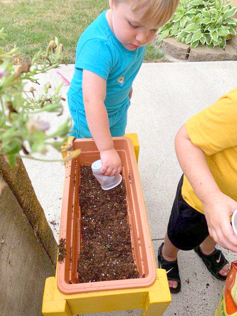 Child filling a planter with soil using a small cup
