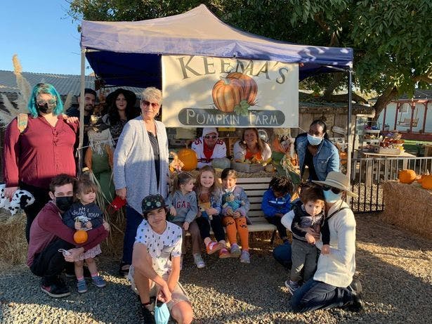 Group of people and children posing in front of a pumpkin farm stand