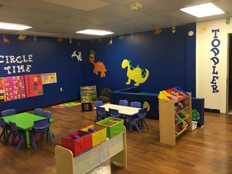 Toddler classroom with tables, chairs, and dinosaur wall decorations