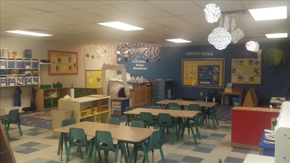 Classroom with small tables and chairs, a play area, and wall decorations