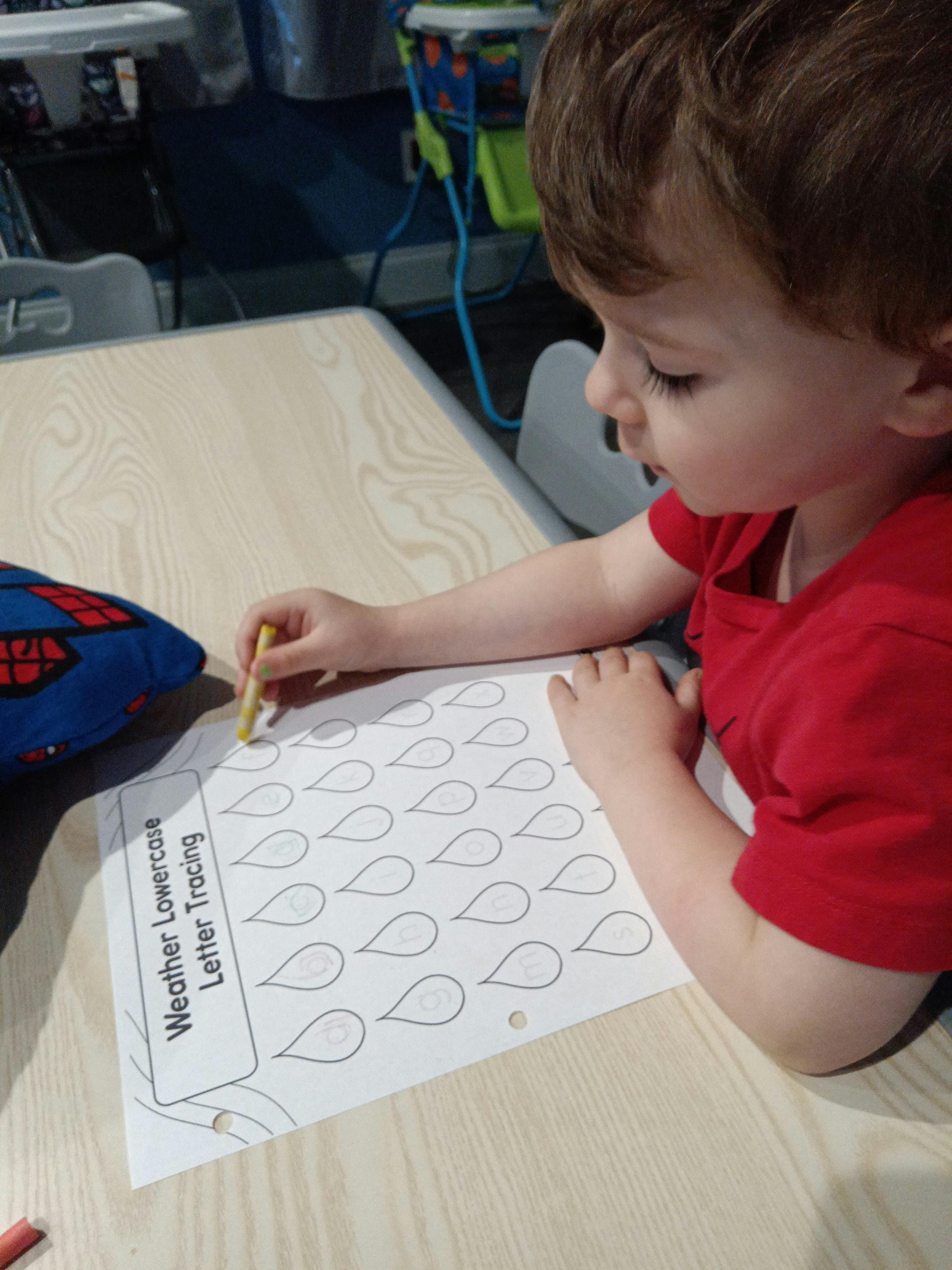 Child tracing letters on a worksheet with a yellow crayon
