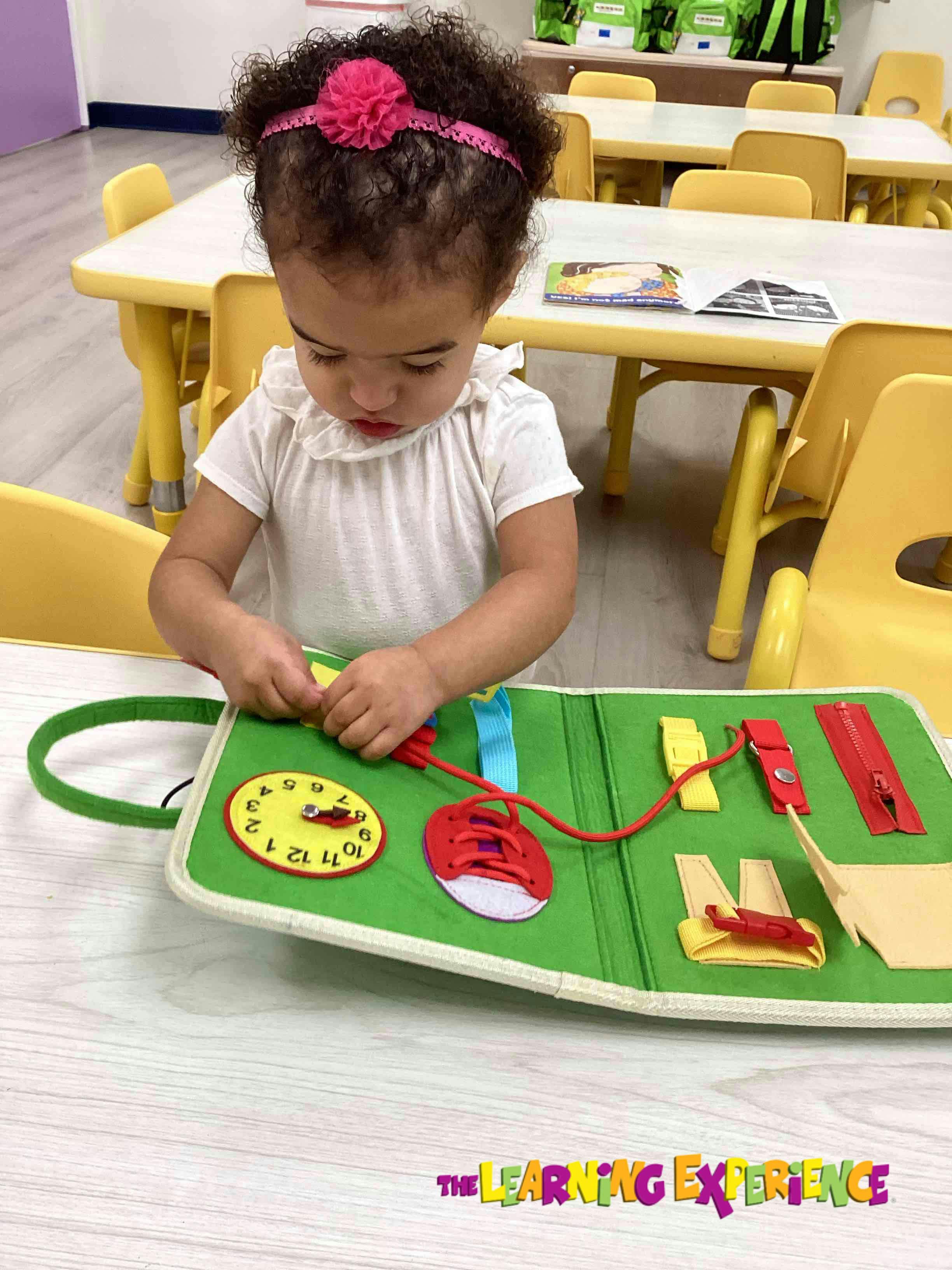 Child playing with a green activity board with a clock, shoelace, and zippers