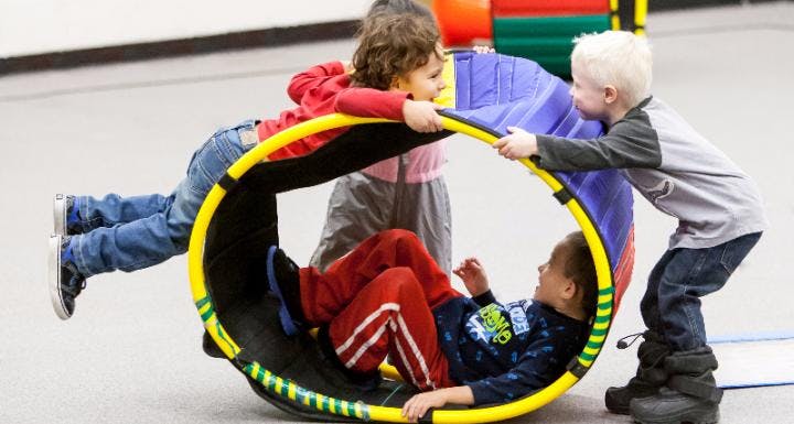 Three children playing with a large circular toy