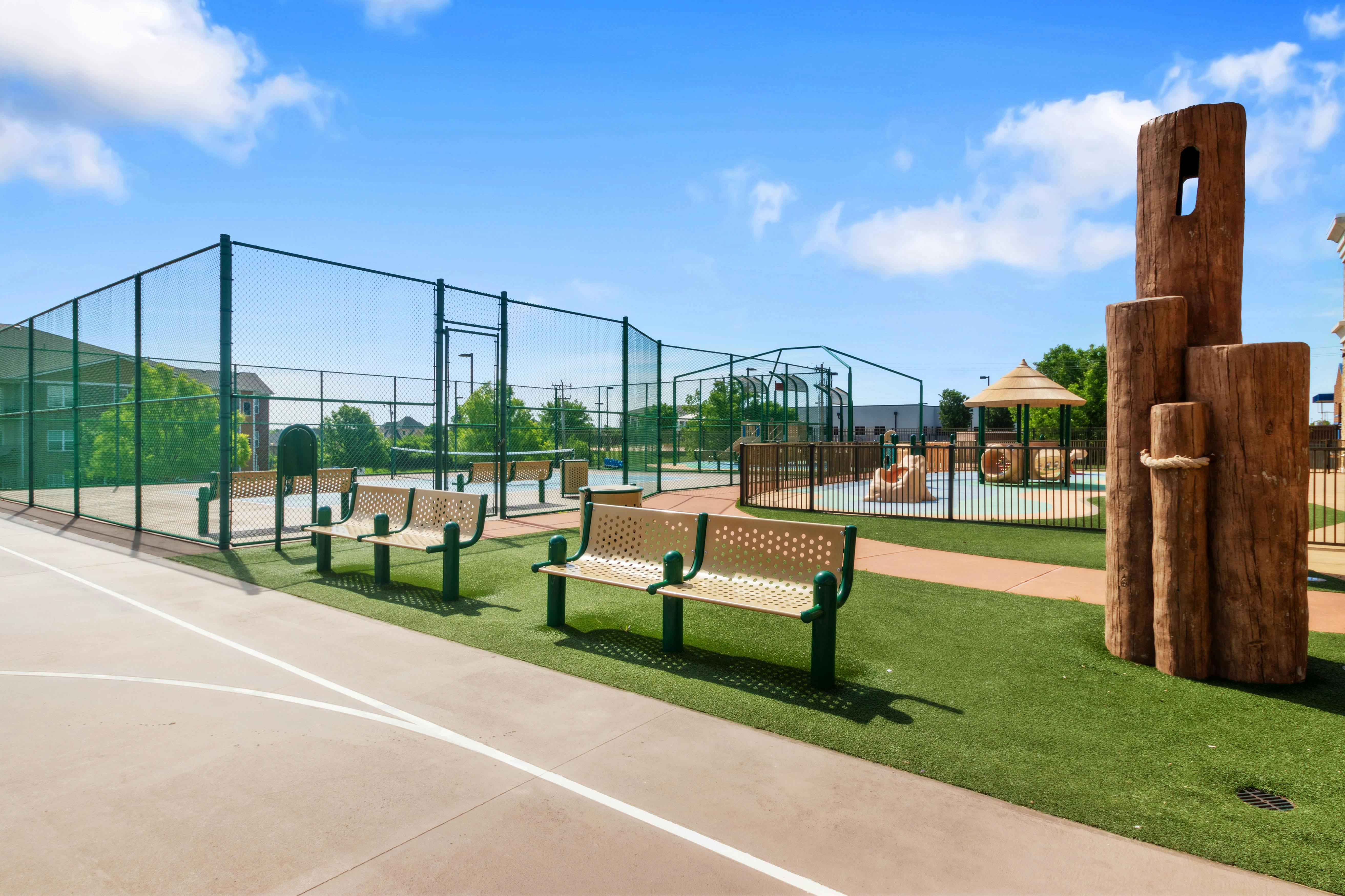 Outdoor recreation area with benches, tennis courts, and a fenced-in playground