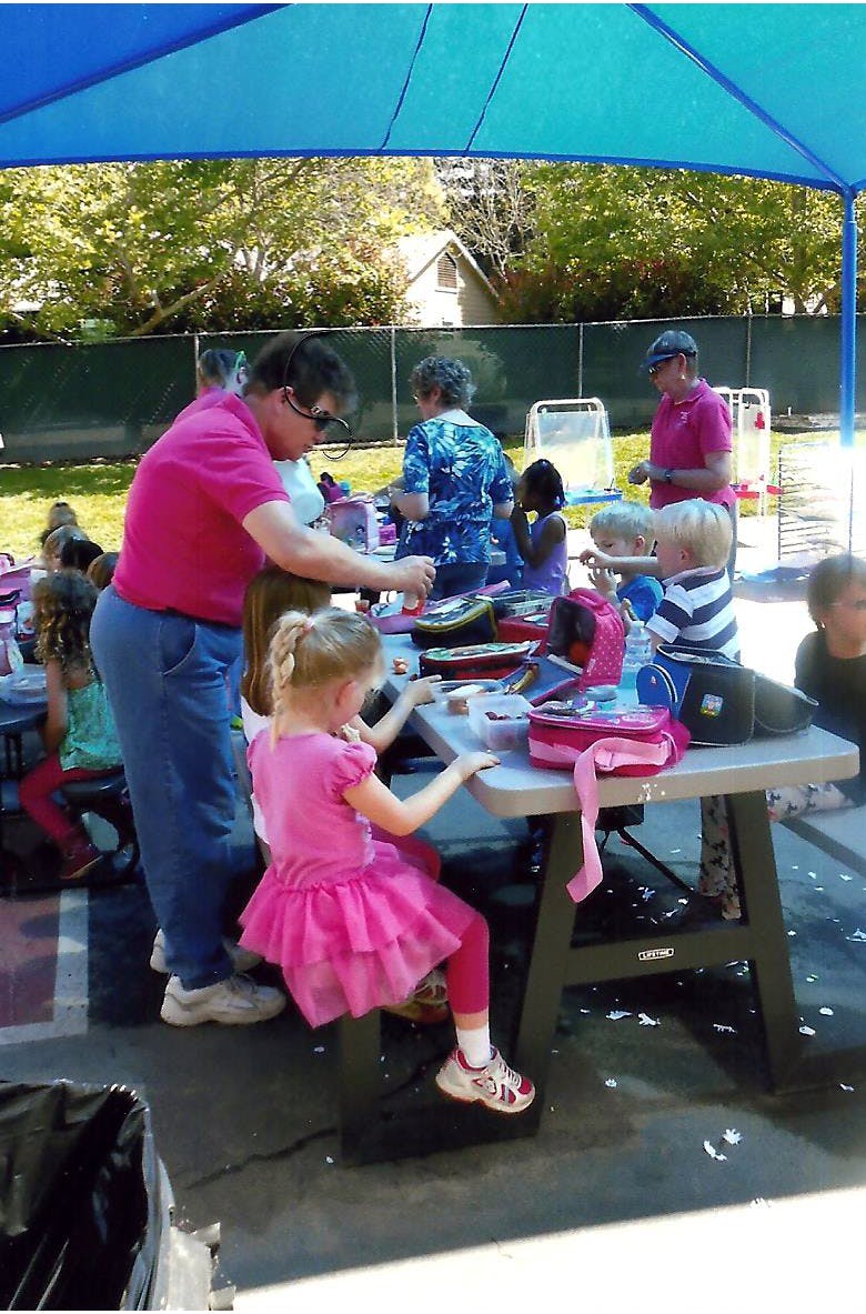 Adults and children gathered around tables under a blue canopy