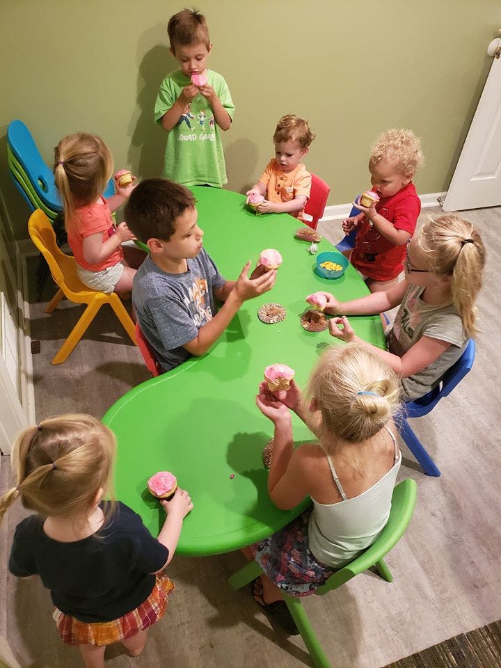 Children sitting around a green table eating cupcakes