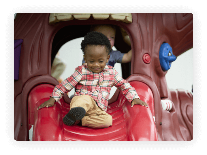 Child on a red slide with another child in the background