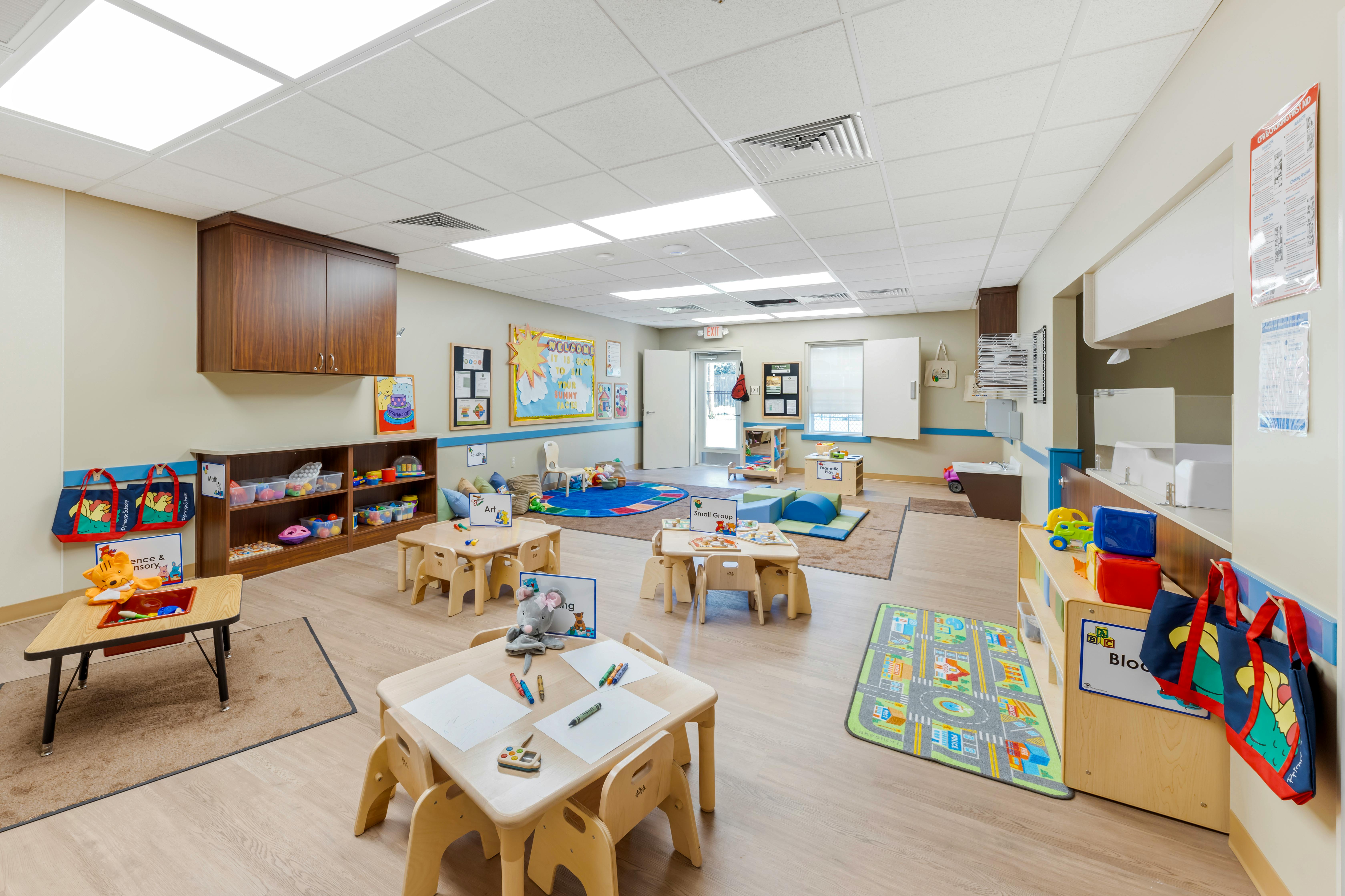 A classroom with small tables and chairs, shelves with toys, and wall decorations