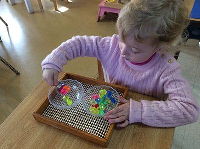 Child sorting colorful objects into bowls on a tray
