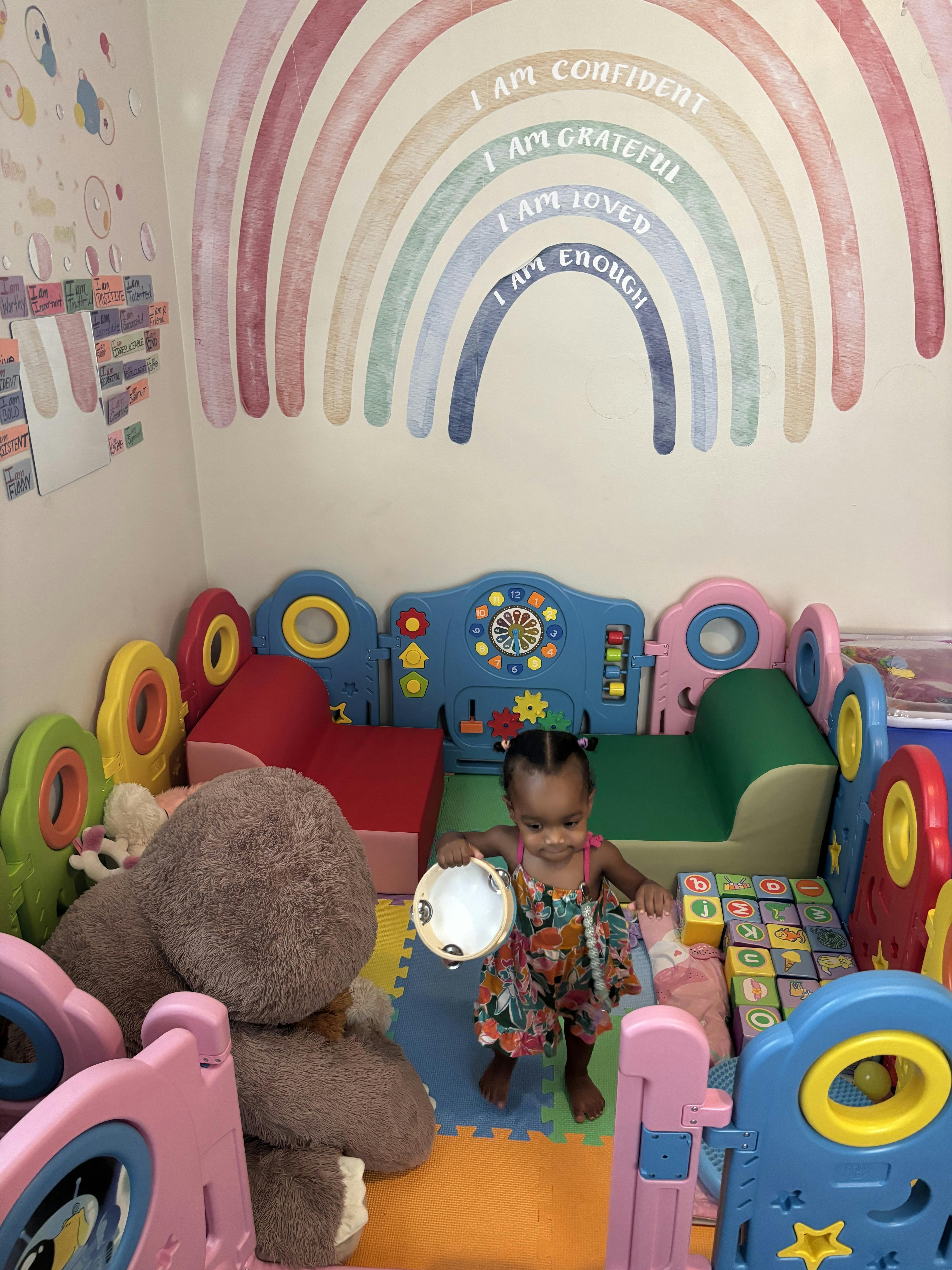 Child holding a tambourine in a play area with a rainbow wall decal