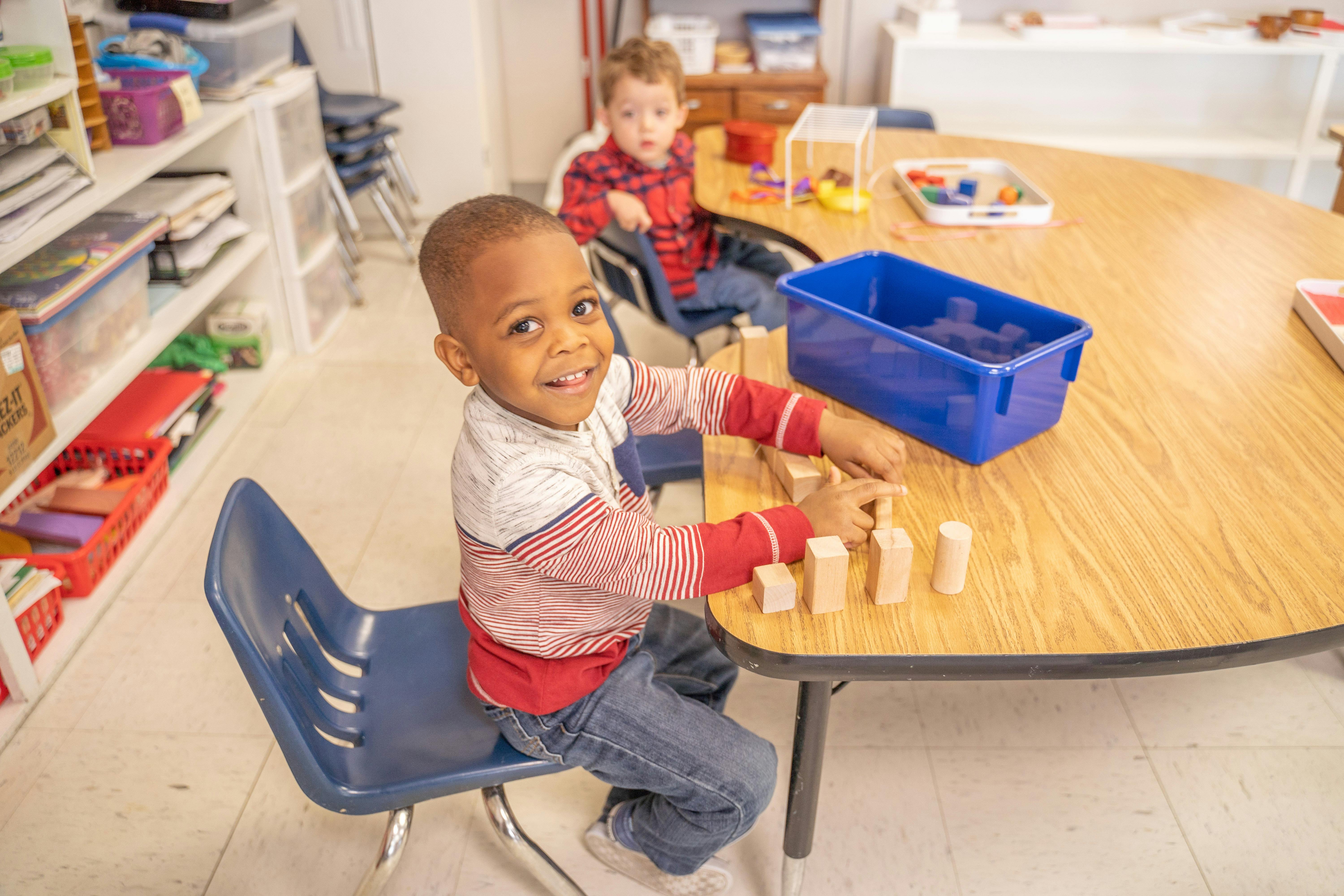 Child playing with wooden blocks at a table in a classroom