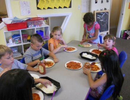 Children making individual pizzas at a table