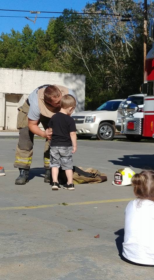 Person in firefighter gear bending down to speak with a child