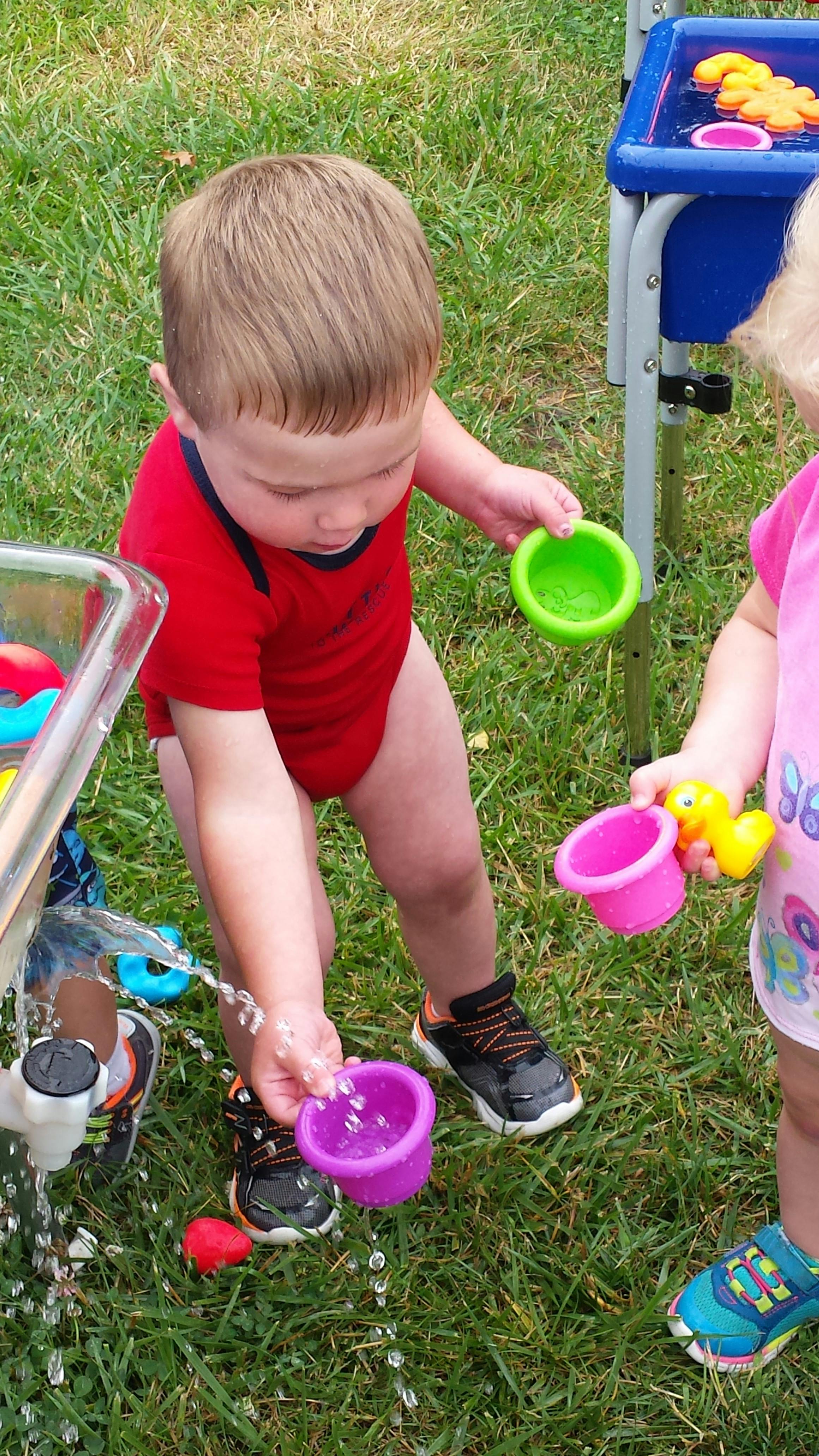 Child playing with water and colorful cups outdoors