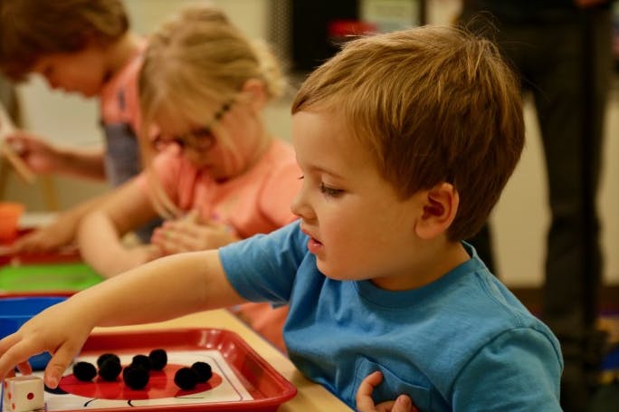 Child in blue shirt playing with black pom-poms on a red tray