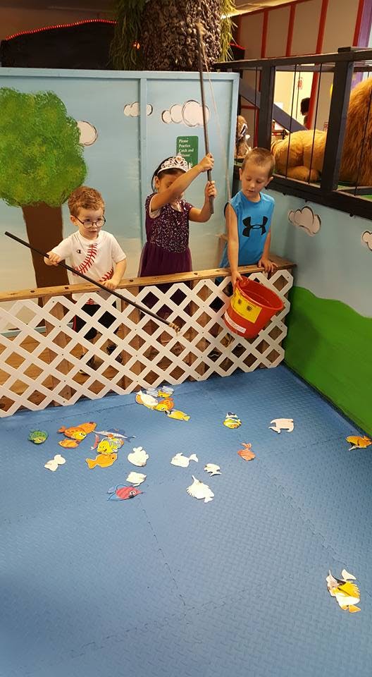 Three children playing a fishing game with toy fish on the floor